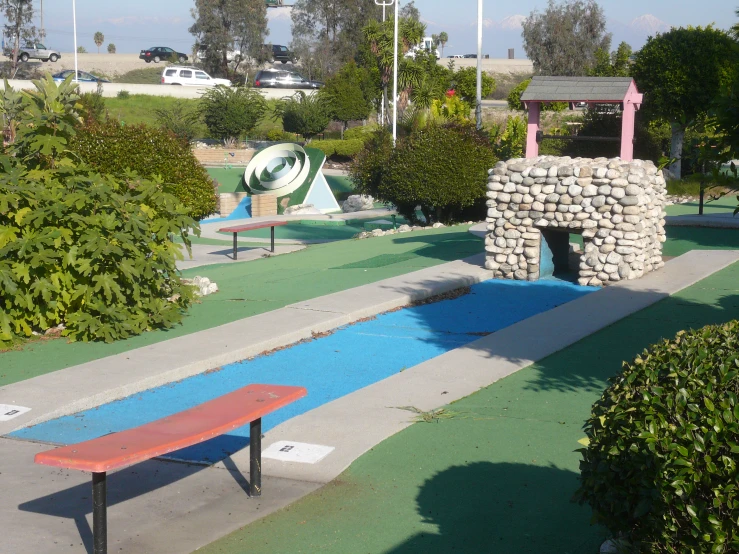 a park with a bench near a pond with stones and a building