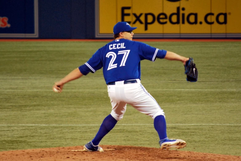 man in blue jersey pitching baseball at outdoor arena