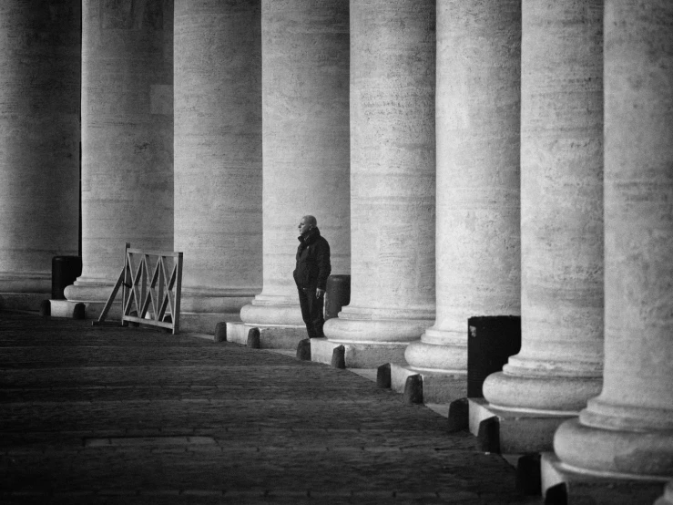 person in a suit walking between a row of large pillars