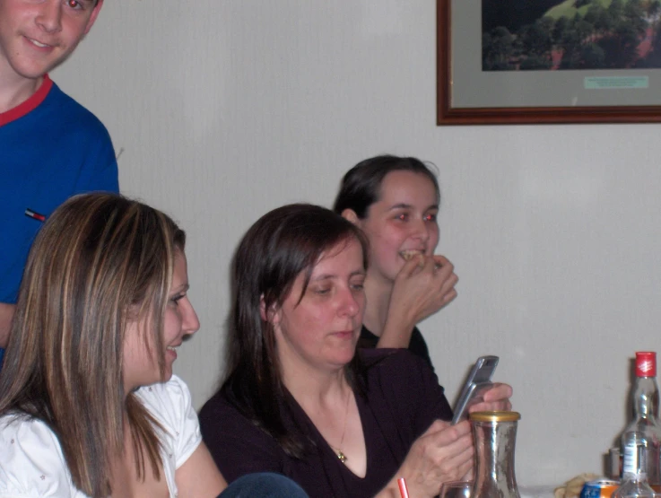 four women are sitting at a table and watching soing on her phone