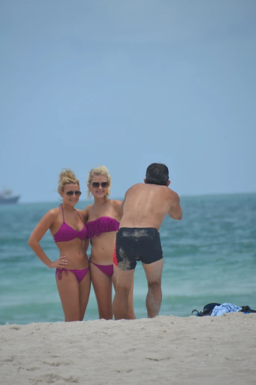 three people in bathing suits posing on the beach