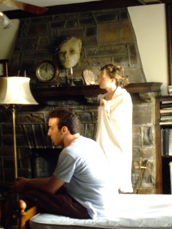 man and a woman sitting on a bed with a fireplace in the background