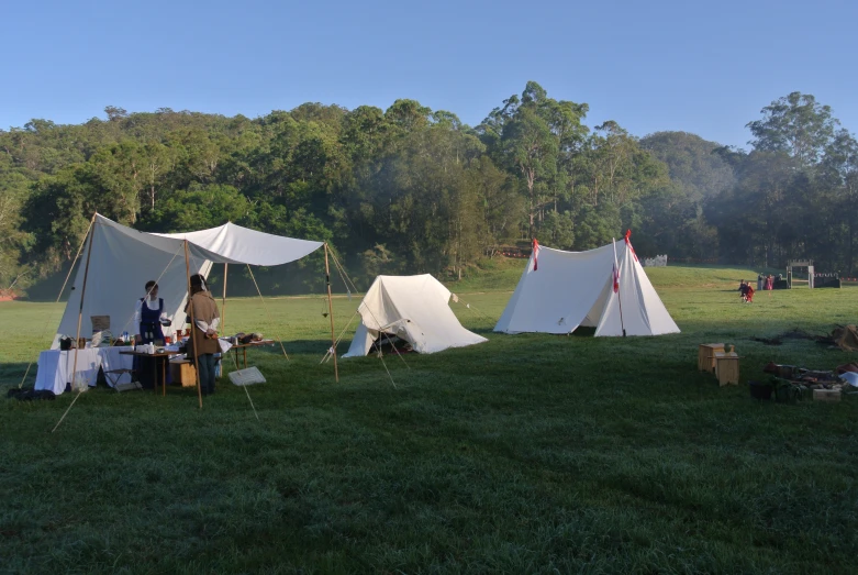 several tents sitting in the middle of a field with people eating and drinking around them