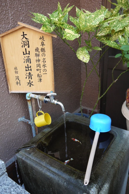 water is running down the side of a concrete fountain with a sign on it and a plastic water cup on the outside of the fountain