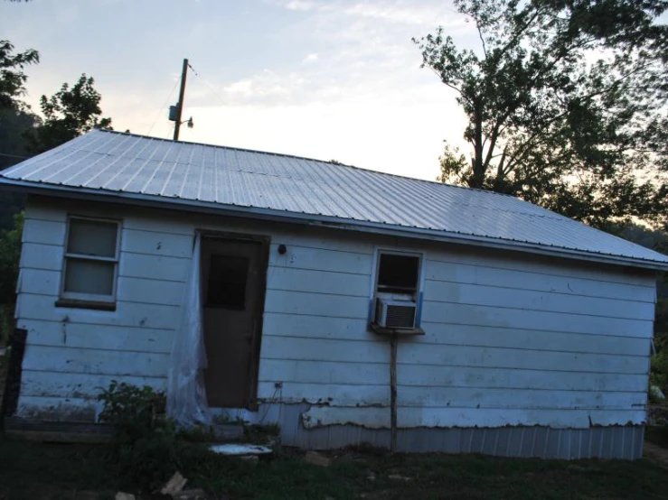 a white shed with a broken door is shown in the evening