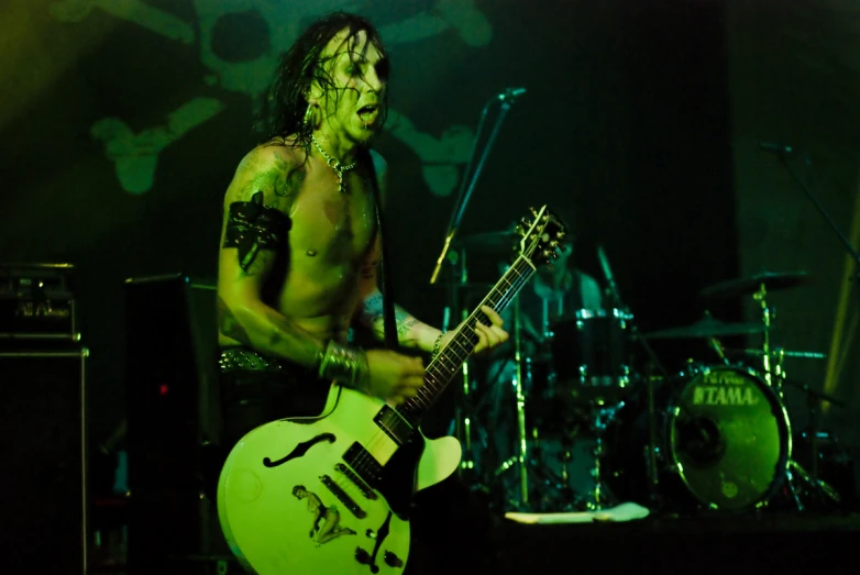 a shirtless guitarist holds his guitar while playing