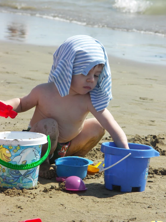 a little boy plays with buckets and a sand toy
