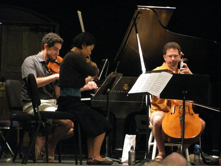 a group of people sitting around a piano and cello