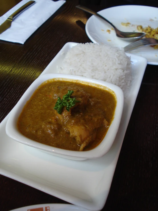 white plate containing rice, chicken curry and gravy on table