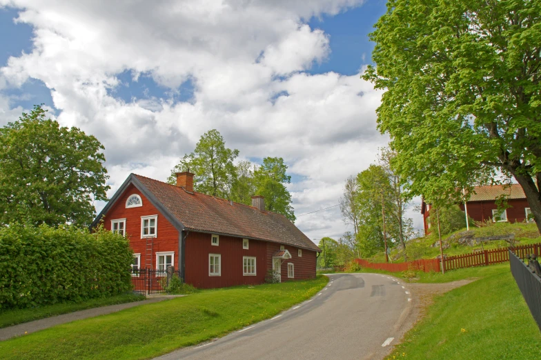 a red house on a road, next to a lush green field