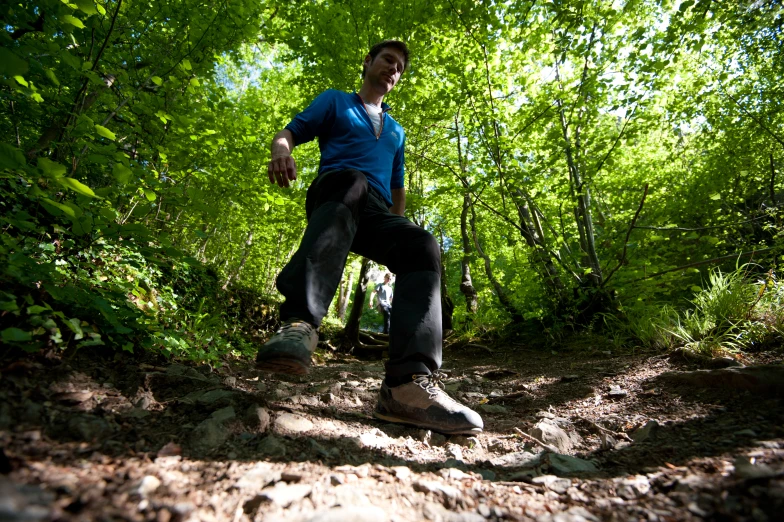 a man in a blue shirt standing on a dirt path with green trees