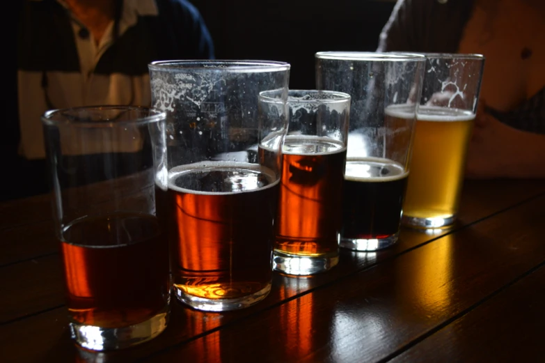 five different glasses of beer sit on a bar