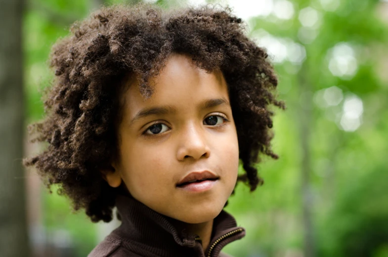 a  with curly hair standing next to trees