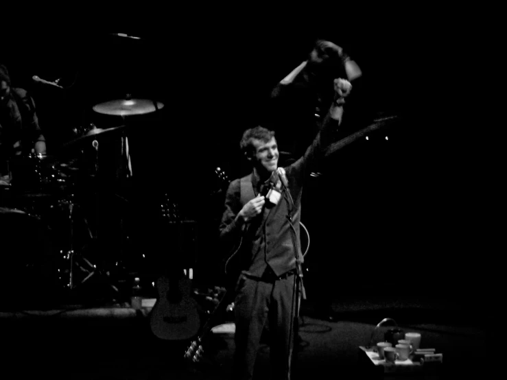 a man in suit and tie standing next to two guitars on stage