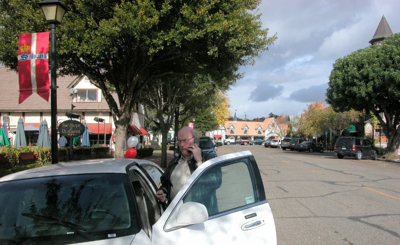 a small white car with the passenger's door open and it's driver in the back seat