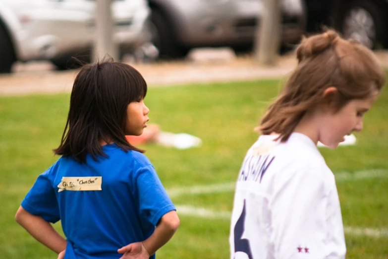 two girls in uniforms stand in front of cars and grassy field