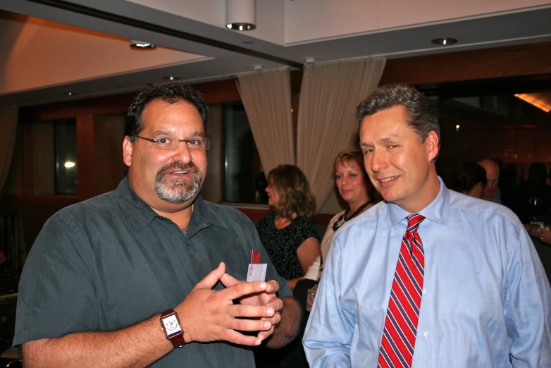 two men with ties are talking in front of some people