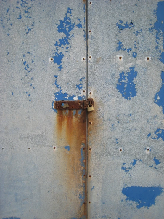 the peeling paint on a building has an old rusted piece of padlock