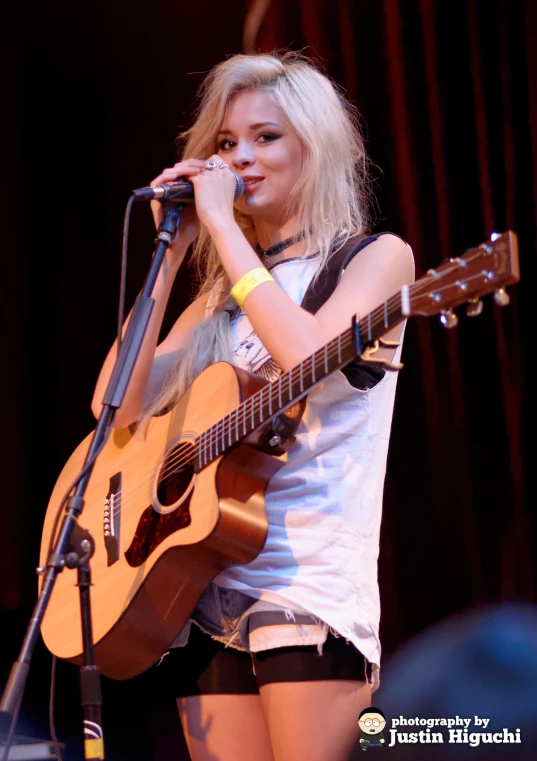 girl with blond hair holding guitar on stage