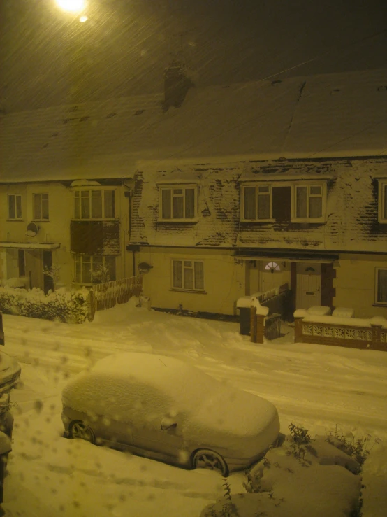 a snowy night with buildings and a car covered in snow