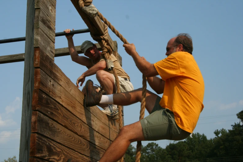 two men are climbing a wooden structure with ropes