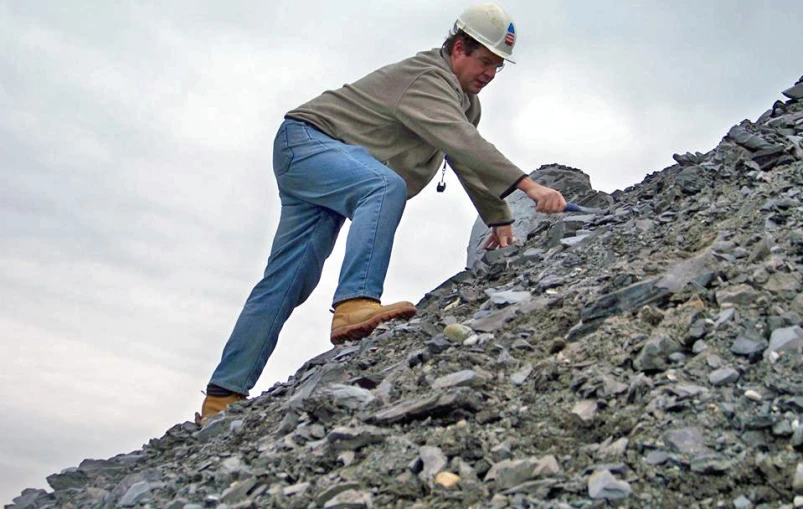 a man with a hat and blue pants walking along a rocky slope