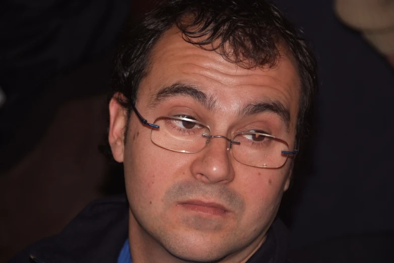 a closeup of a man in glasses and a blue shirt