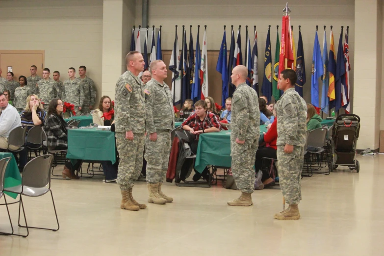 military men in fatigues standing in front of large room full of flags