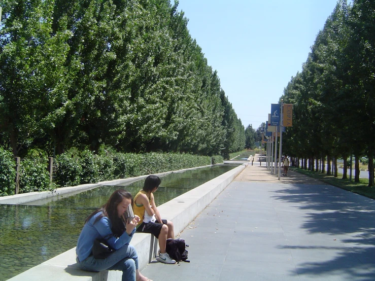 two people sitting on a bench at the end of a walkway by a pond