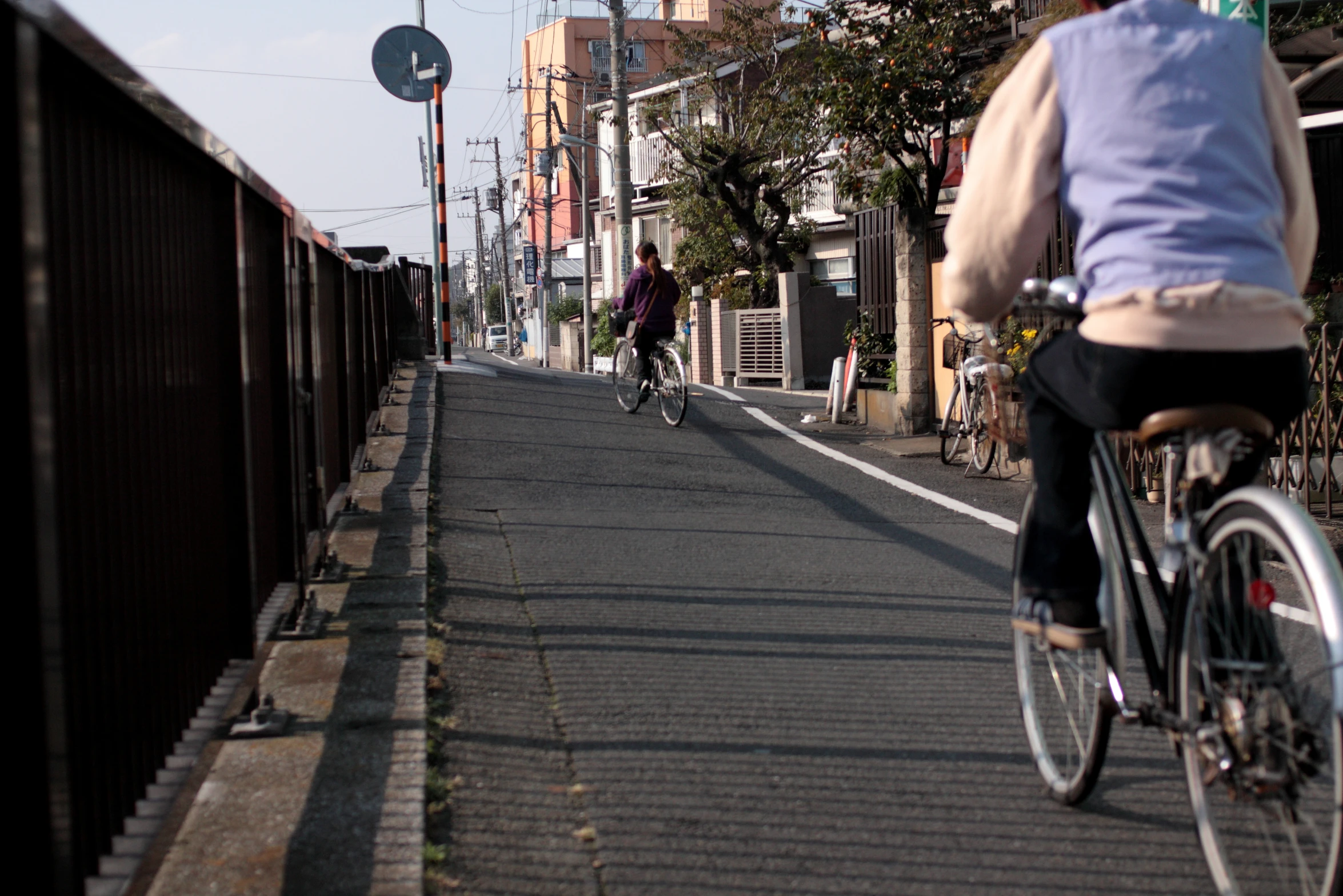 man riding bicycle in street next to brown wooden fence