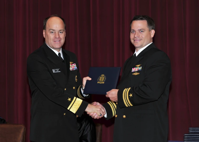 two military officers with medals holding a blue plaque