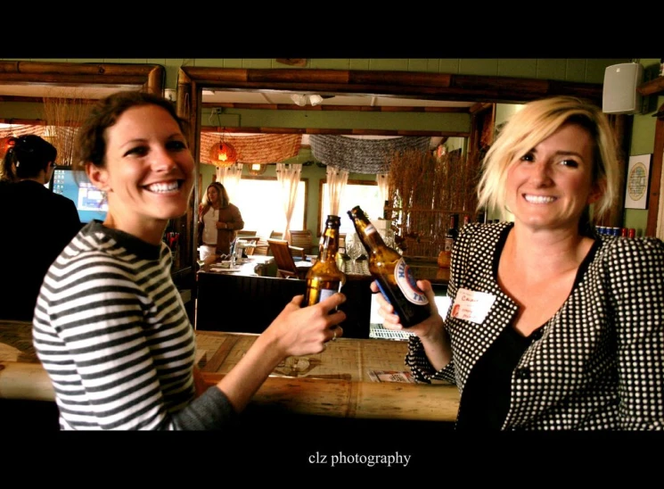 two women with wine bottles are standing and smiling