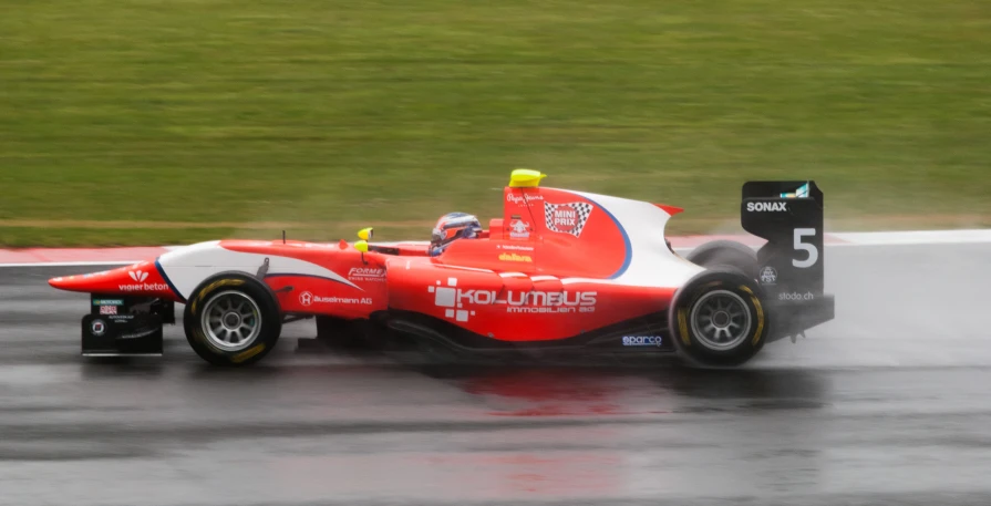 red race car driving on wet track with rain coming from front wheel