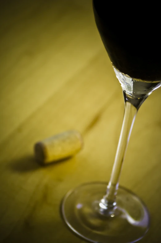 the glass with the wine is next to the cork of a single g