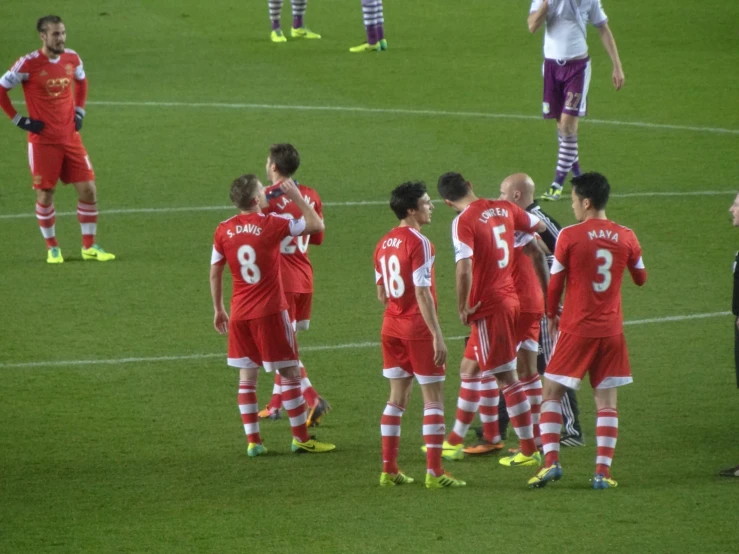 a group of soccer players in red and white uniforms talking