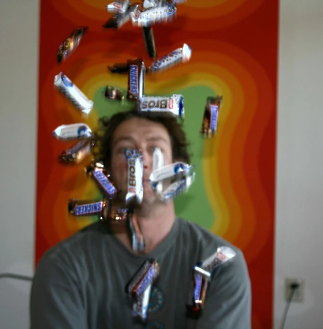 a man making a weird face with assorted soda bottles flying over his head