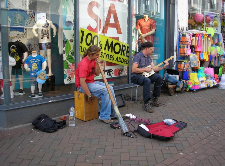 two people sit on the street holding guitars and talking