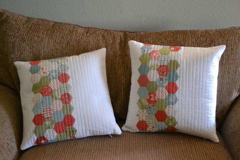 two decorative pillows placed on the arm of a brown couch