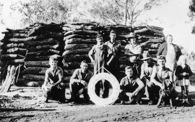 an old black and white po of men standing by stacked logs