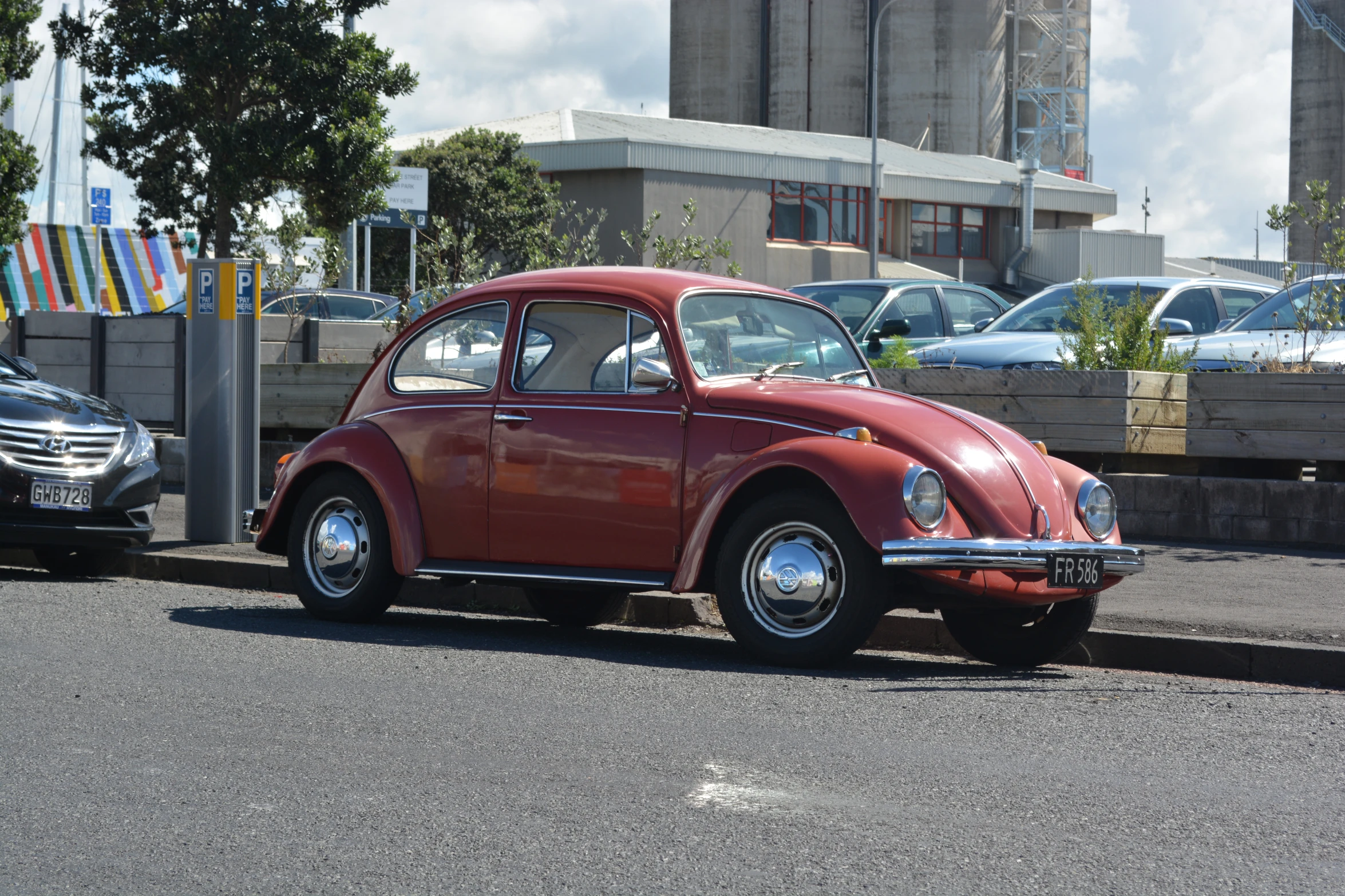 red volkswagen beetle parked on the curb next to other cars