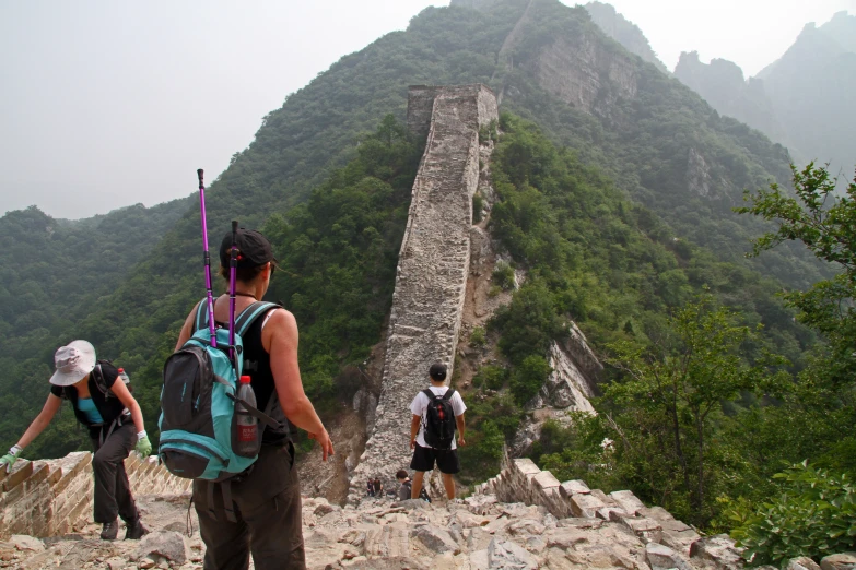 three people standing on a great wall of stone with backpacks