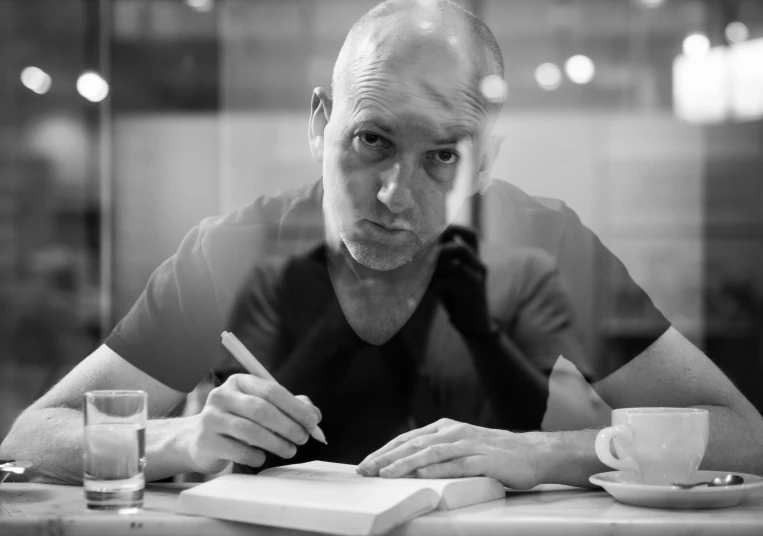 an older man sits at a table writing