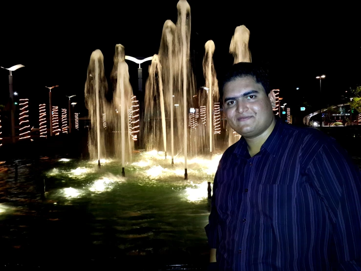 a man standing in front of water fountain at night
