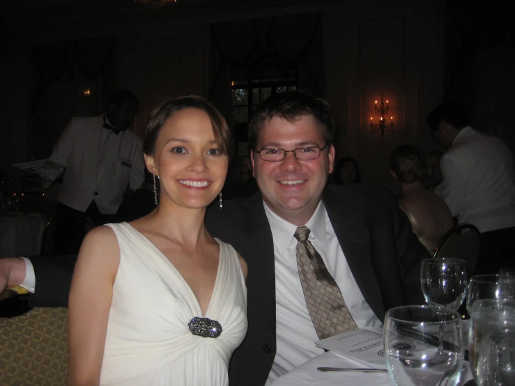 two people wearing glasses, one woman in a white dress