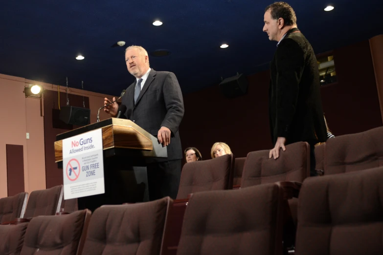 two men stand at a podium with a no smoking sign