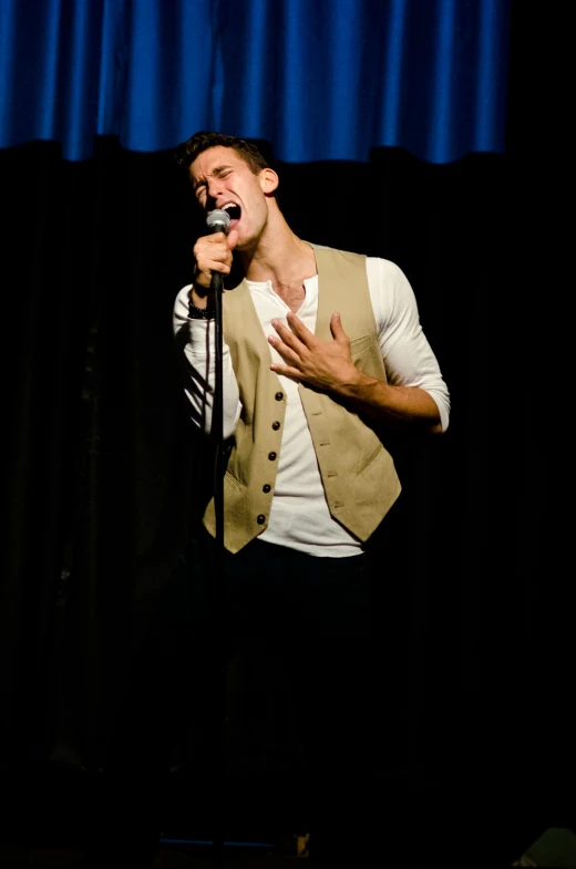 a man singing into a microphone in front of a curtain