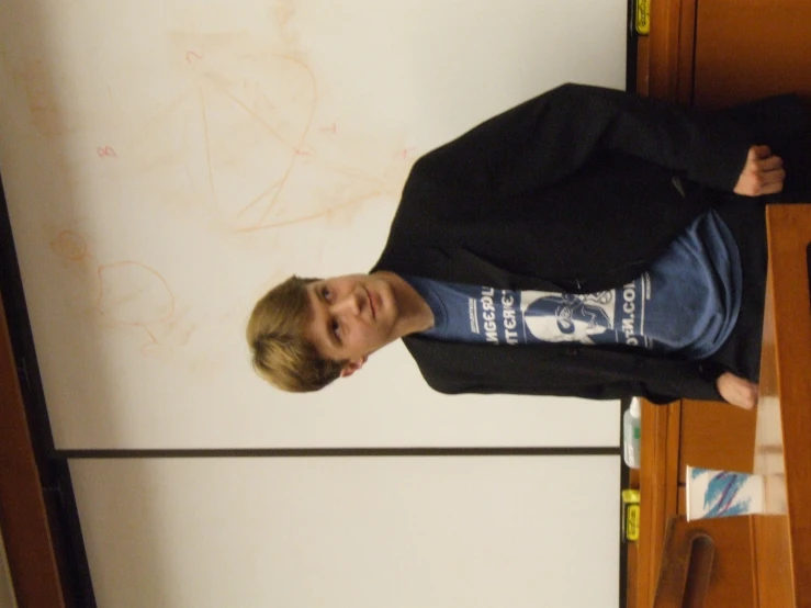 a little boy wearing a black sweatshirt and shorts, next to a refrigerator