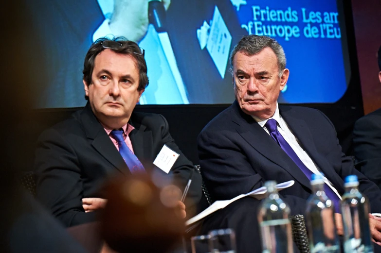 three men sitting together at a table in suits