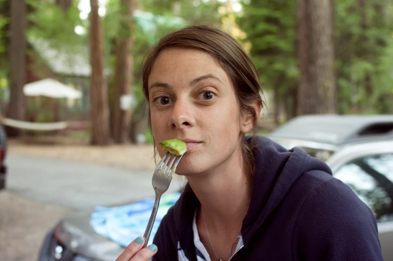 a girl eats a piece of apple on a fork outside
