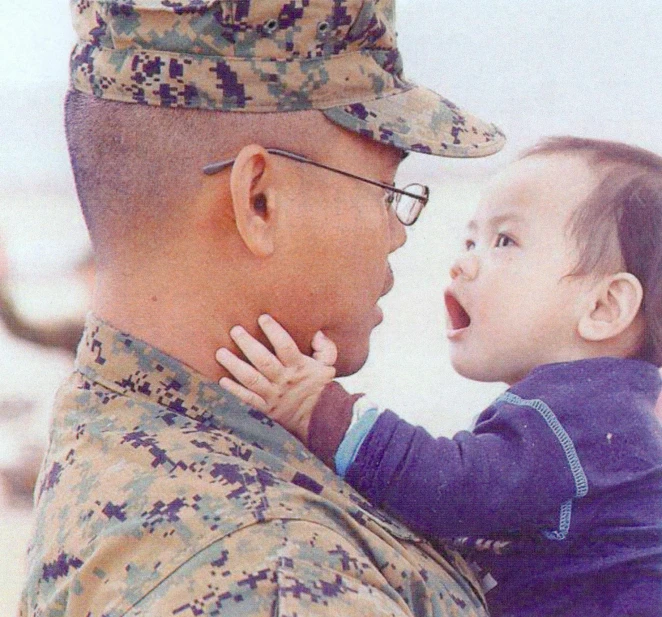 a man in army clothes holds a little child